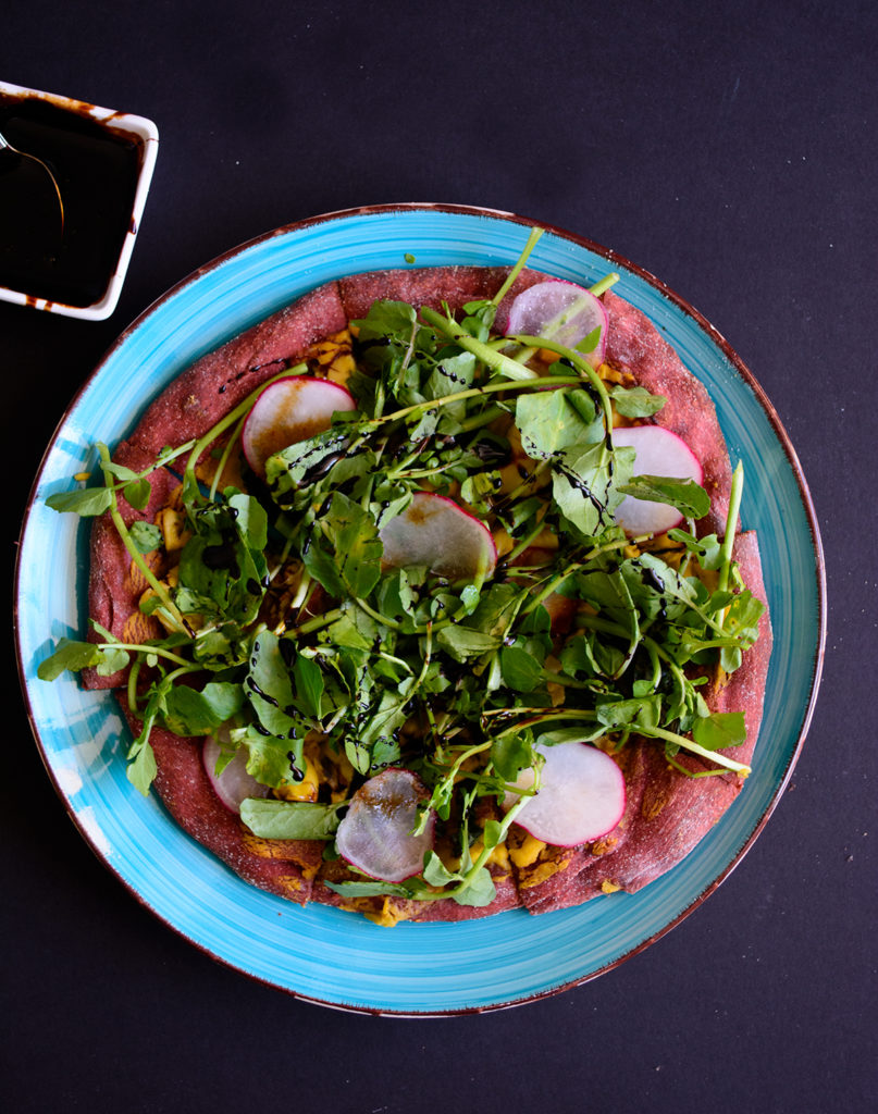 Beets and Greens Ackee Flatbread: Beetroot pizza dough topped with ackee and butternut squash cream, ackees, marinated greens and finished with watercress, radish, garlic oil and balsamic glaze, it's a mouthful of ultimate deliciousness